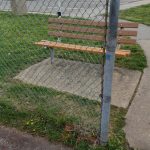 Chain-link fence enclosing a small park area with wooden benches and gravel ground.