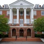 Brick building with white columns and portico, featuring multiple windows and trees.