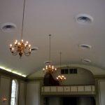 Ornate chandeliers hang from a white ceiling above an arched interior space.