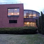 Modern brick building with large curved glass facade and manicured green landscaping.