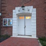 Brick building entrance with white stone surround and double doors.