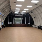 Large, arched indoor venue with a wooden floor and stage setup for events.