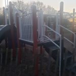 Playground equipment silhouetted against a bright, hazy sunset sky.