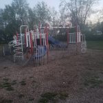 Children's playground equipment with a slide, surrounded by a metal fence on a grassy area.
