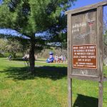 Park sign at Willshire Park with playground equipment visible in the grassy background.