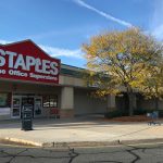 Staples office superstore with a large yellow-leafed tree in front on a sunny day.