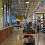 Interior view of a large retail store with aisles, shelves stocked with goods, and natural light from large windows.