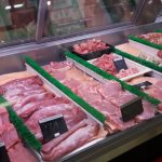 Butcher shop display case filled with various cuts of raw, fresh pork and meat.