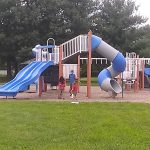 Children play on a colorful playground featuring slides and a blue spiral tube.