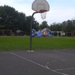 Basketball hoop on a court with playground equipment and trees in the background.