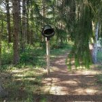 Outdoor forest path with a hanging metal gong on a wooden post.