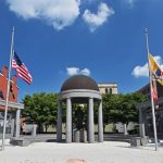 Outdoor plaza with a central dome, flanked by buildings and American flags under a blue sky.