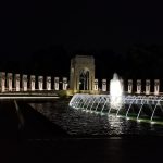 Nighttime fountain display with illuminated arches and water jets against a dark background.