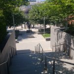 Campus courtyard with trees, walkways, and modern architecture under a bright sky.