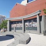 Modern building facade with large mural, curved concrete plaza in foreground.