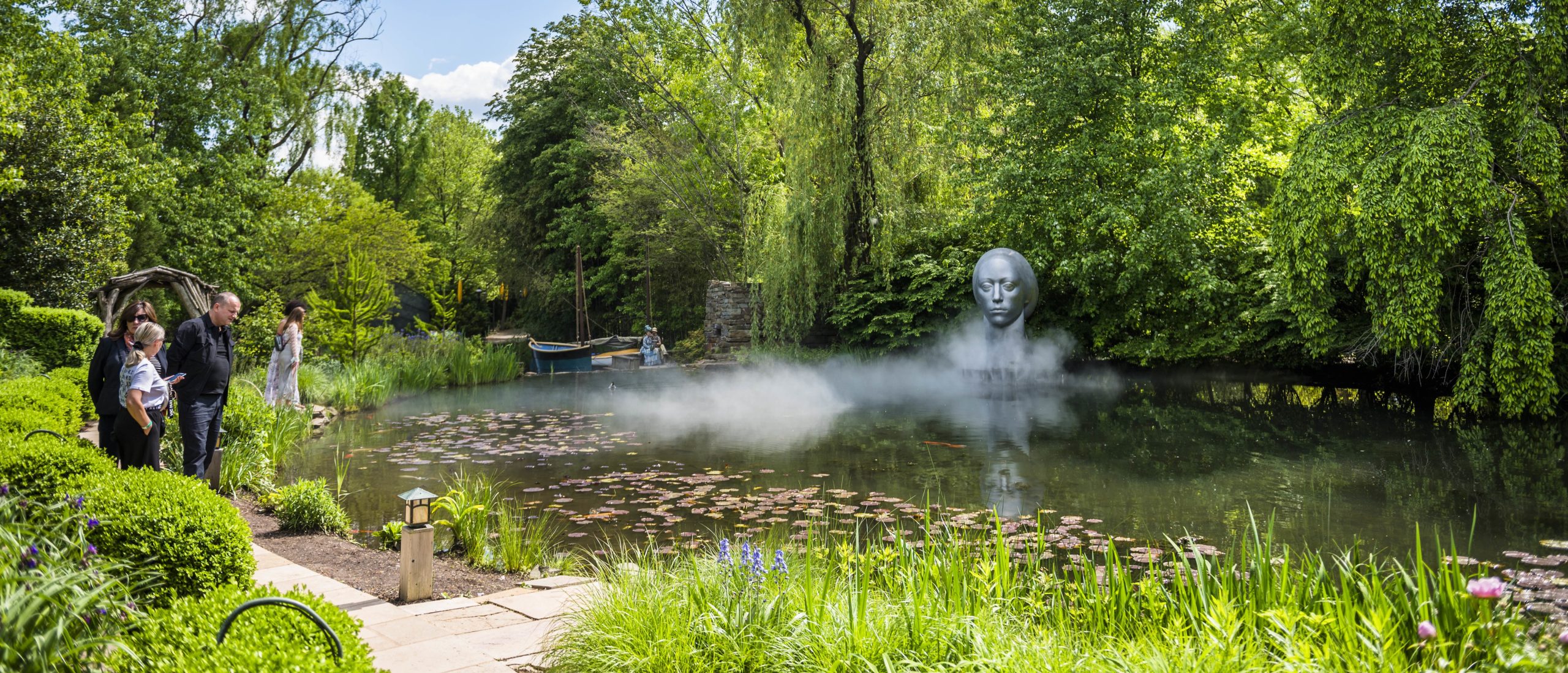 people overlooking artwork across a river at Grounds for Sculpture in Hamilton New Jersey